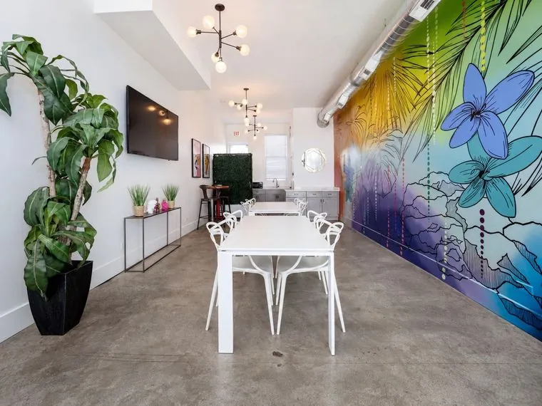 Nala’s Party Room with white tables, a tropical mural and a wall-mounted TV